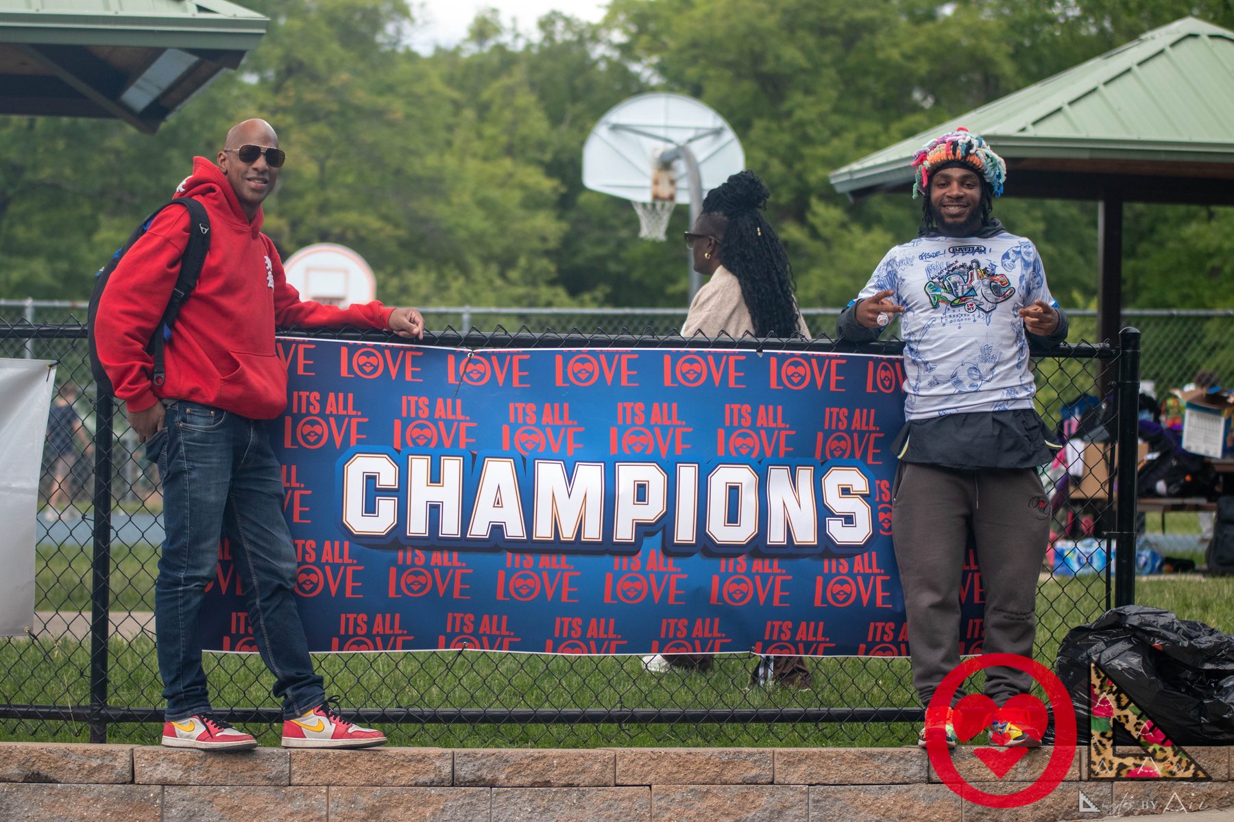 Two members of the It's All Love community beside the CHAMPIONS banner at the Family & Friends BBQ